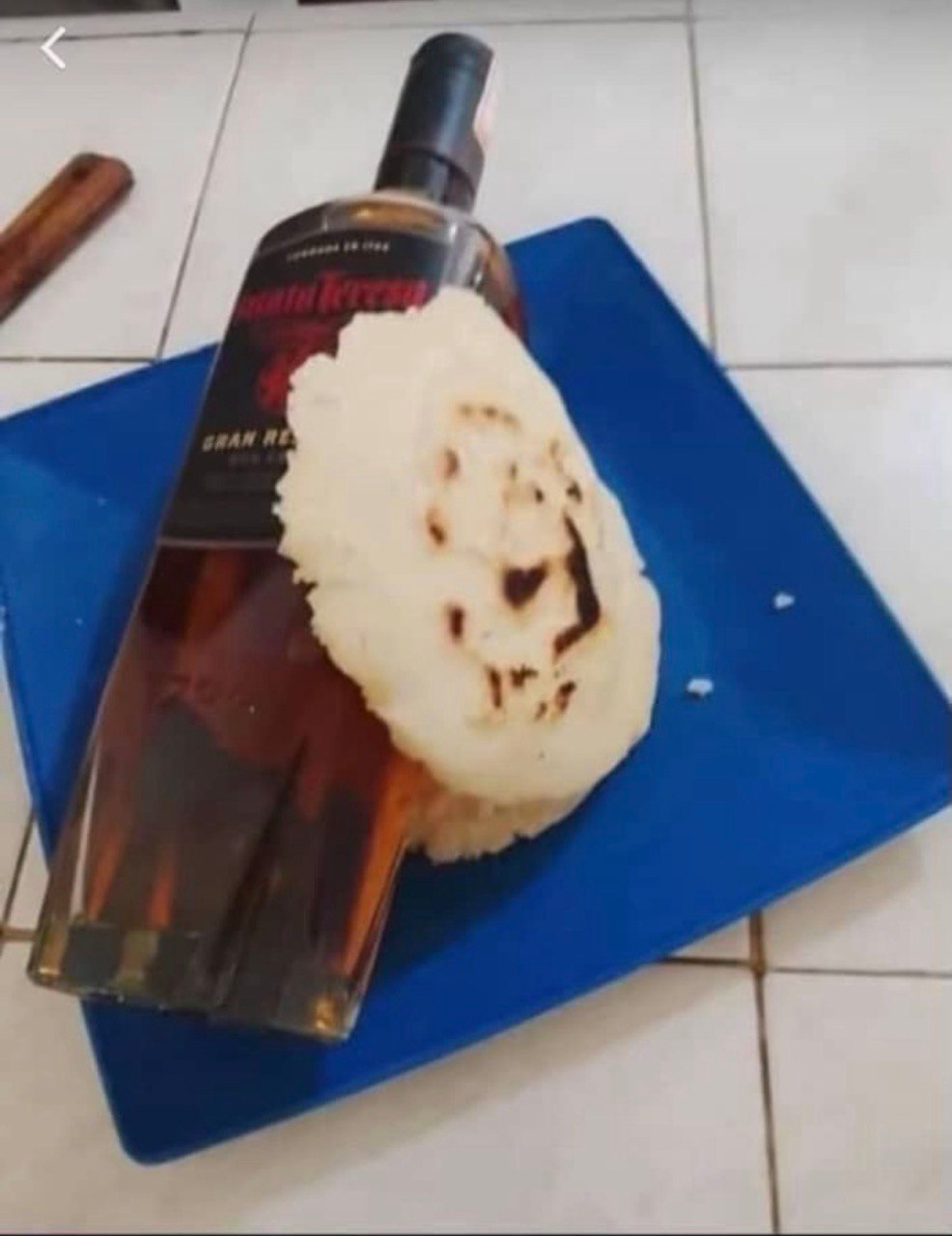 A bottle of dark rum lying on a blue plate next to a toasted arepa
